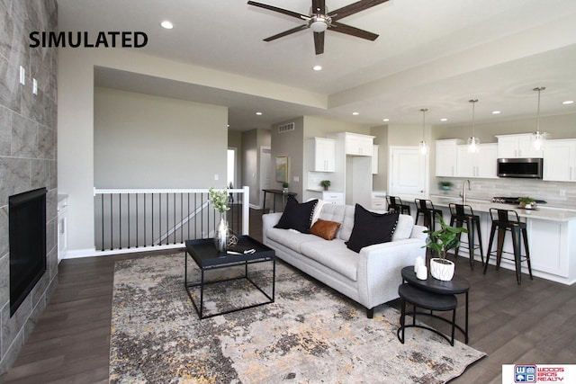 living room with ceiling fan, sink, dark wood-type flooring, and a tile fireplace