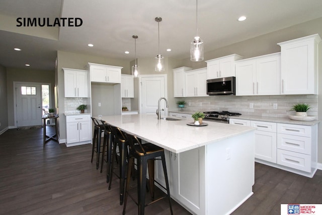 kitchen with appliances with stainless steel finishes, a center island with sink, white cabinetry, and decorative light fixtures