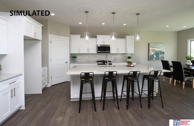 kitchen featuring stainless steel appliances, decorative light fixtures, dark hardwood / wood-style floors, white cabinetry, and an island with sink