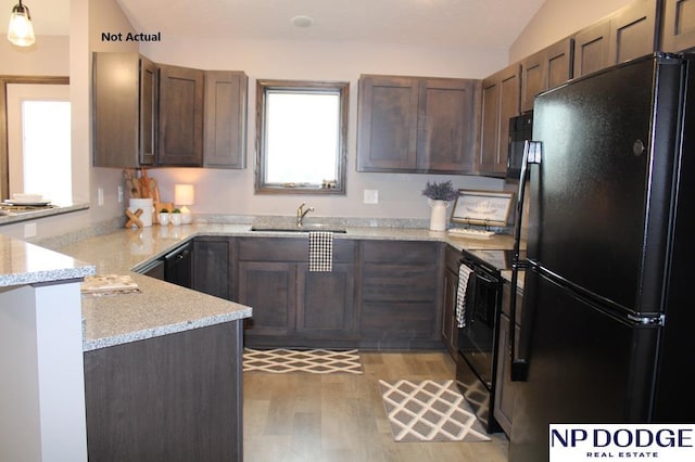 kitchen with kitchen peninsula, light stone countertops, black appliances, light hardwood / wood-style floors, and lofted ceiling