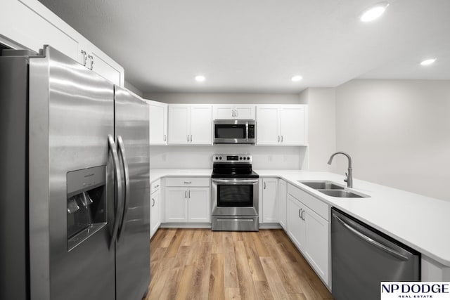 kitchen featuring white cabinetry, sink, light hardwood / wood-style flooring, kitchen peninsula, and appliances with stainless steel finishes