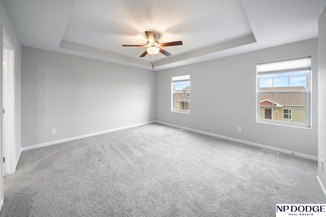 unfurnished room featuring a raised ceiling, ceiling fan, and carpet floors