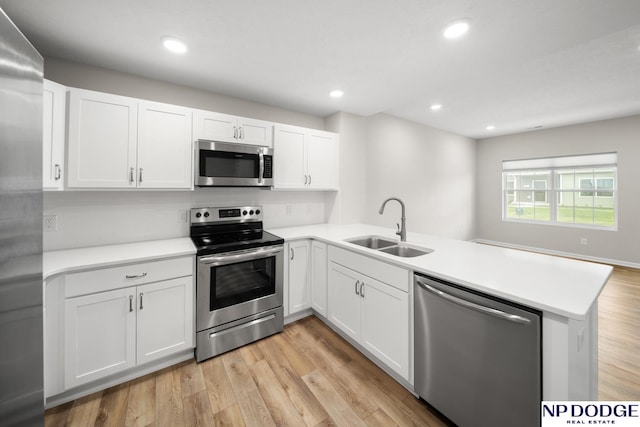 kitchen with kitchen peninsula, stainless steel appliances, sink, light hardwood / wood-style flooring, and white cabinetry