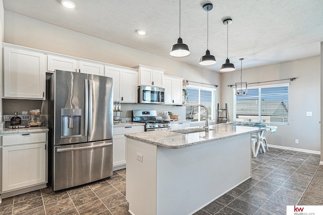 kitchen with appliances with stainless steel finishes, a kitchen island with sink, sink, pendant lighting, and white cabinetry