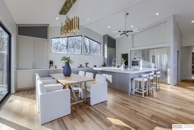 dining space featuring beamed ceiling, high vaulted ceiling, light hardwood / wood-style floors, and an inviting chandelier