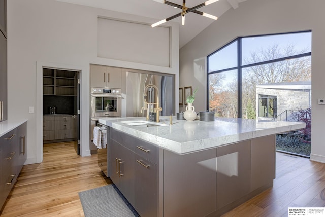 kitchen featuring gray cabinetry, sink, light stone countertops, light wood-type flooring, and an island with sink