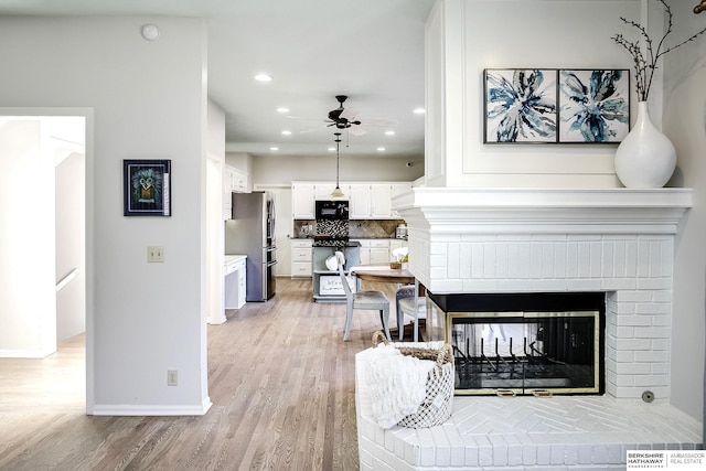 living room with light hardwood / wood-style floors, a brick fireplace, and ceiling fan