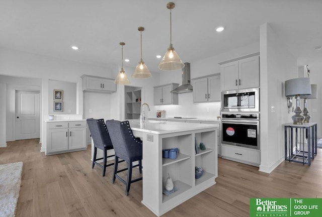 kitchen with light hardwood / wood-style floors, wall chimney range hood, a kitchen island with sink, and black cooktop