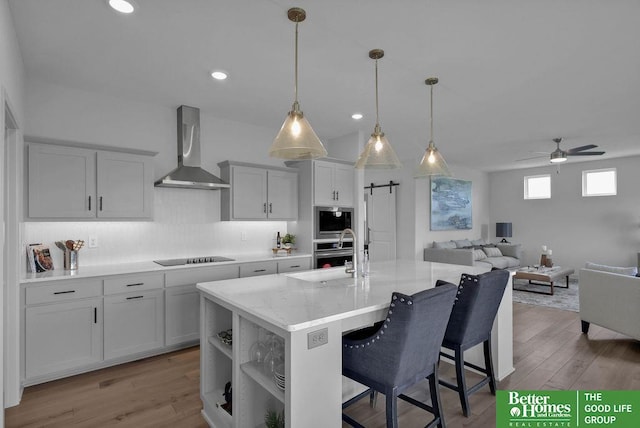 kitchen with a kitchen bar, light wood-type flooring, wall chimney range hood, a barn door, and a center island with sink