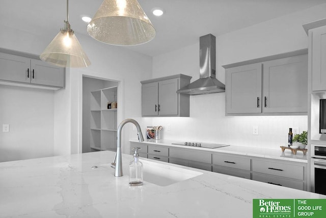 kitchen with black electric stovetop, sink, wall chimney range hood, decorative light fixtures, and gray cabinets