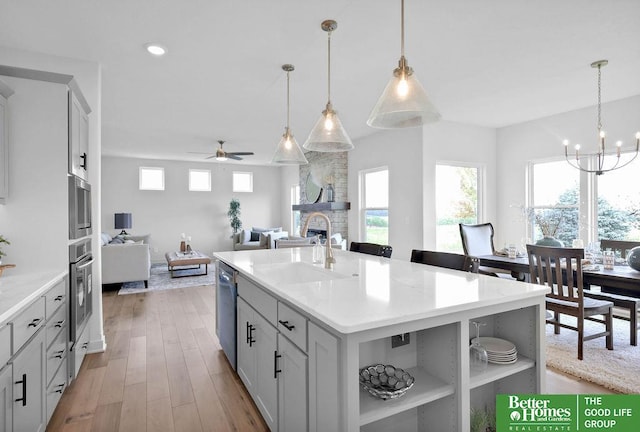 kitchen featuring stainless steel appliances, pendant lighting, light hardwood / wood-style flooring, a stone fireplace, and an island with sink