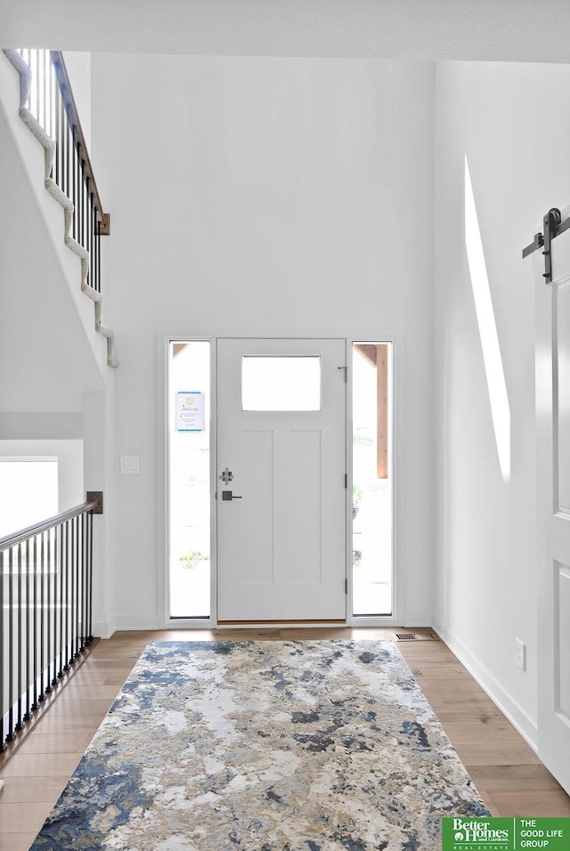 entrance foyer with a barn door, a towering ceiling, and light hardwood / wood-style flooring