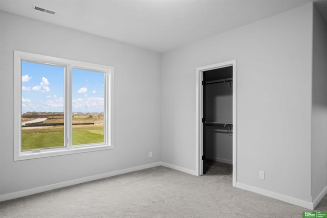 unfurnished bedroom featuring light colored carpet, a walk in closet, and a closet