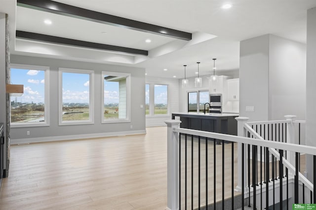 kitchen featuring sink, decorative light fixtures, a kitchen island with sink, white cabinets, and light wood-type flooring