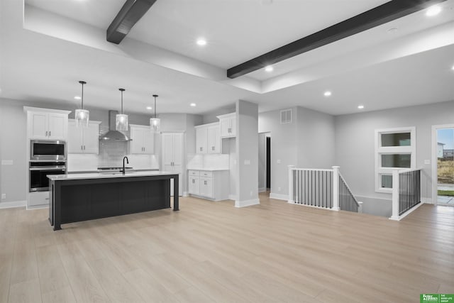 kitchen featuring white cabinets, an island with sink, light hardwood / wood-style floors, and wall chimney range hood