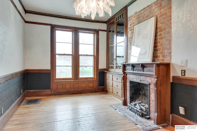 unfurnished living room with a chandelier, ornamental molding, a fireplace, and light hardwood / wood-style flooring