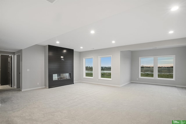 unfurnished living room featuring a large fireplace, light colored carpet, and plenty of natural light