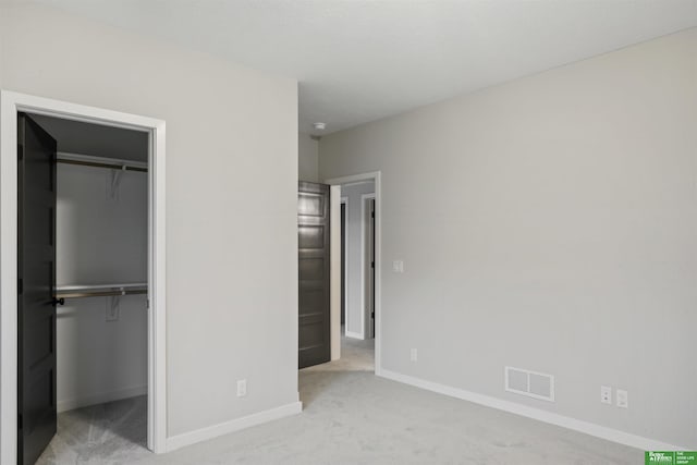 unfurnished bedroom featuring a walk in closet, light carpet, and a closet