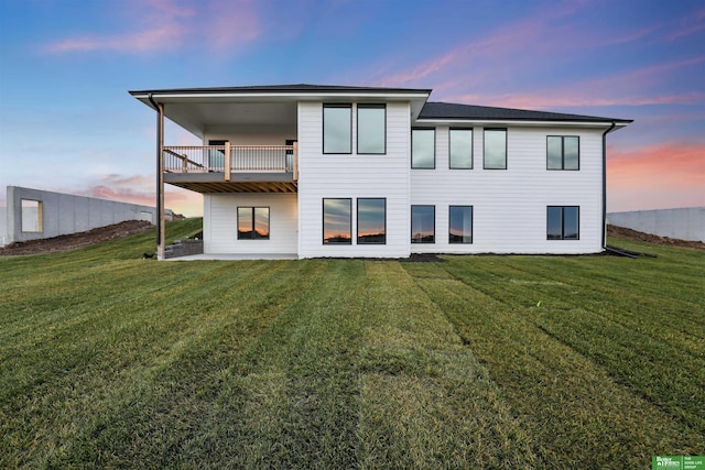 back house at dusk with a lawn and a balcony