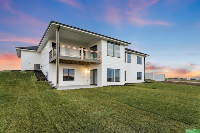 back house at dusk featuring a balcony, a yard, a patio, and central AC