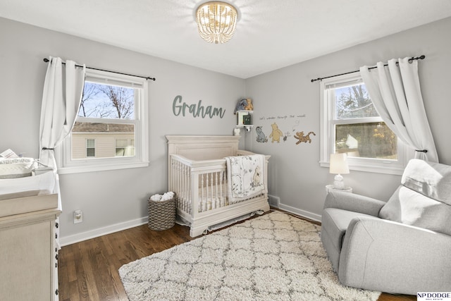 bedroom with a crib, dark hardwood / wood-style flooring, and a notable chandelier