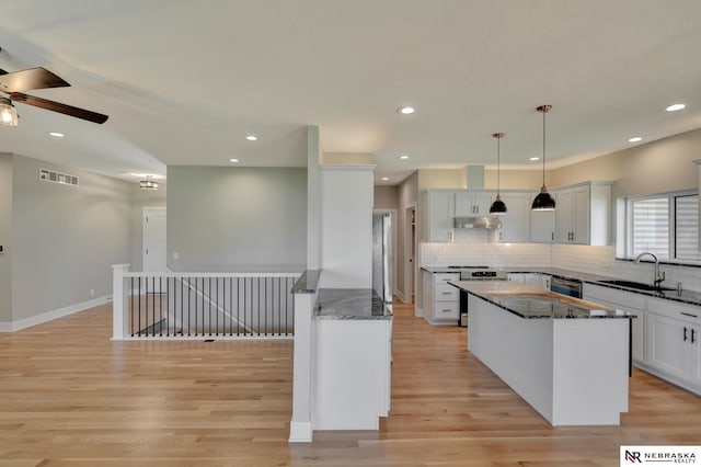 kitchen with a center island, white cabinets, sink, light wood-type flooring, and decorative light fixtures