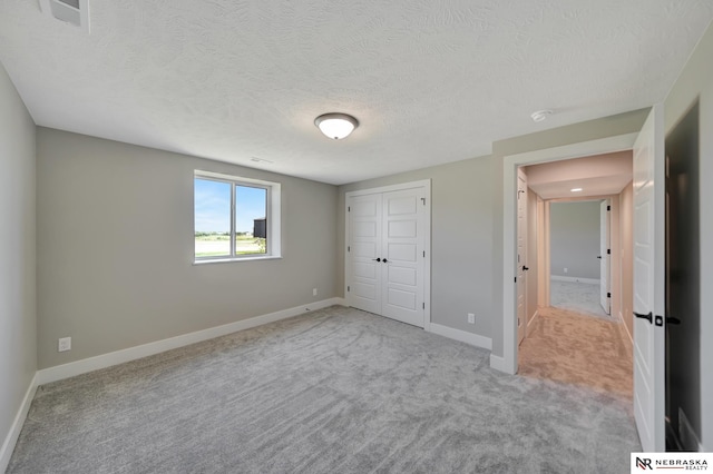 unfurnished bedroom featuring light carpet, a textured ceiling, and a closet