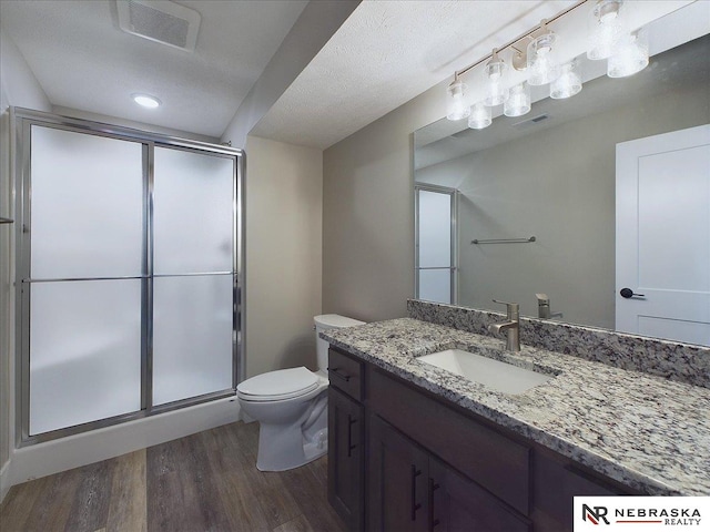 bathroom with vanity, a textured ceiling, a shower with door, hardwood / wood-style flooring, and toilet