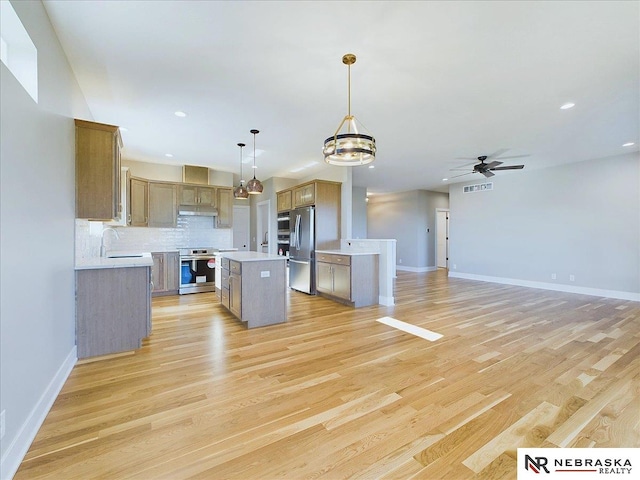 kitchen featuring ceiling fan with notable chandelier, light hardwood / wood-style flooring, appliances with stainless steel finishes, decorative light fixtures, and a kitchen island