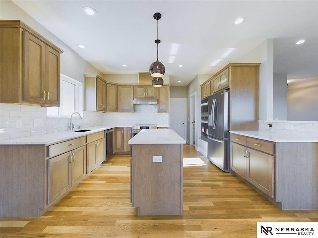 kitchen with sink, hanging light fixtures, light wood-type flooring, a kitchen island, and stainless steel appliances