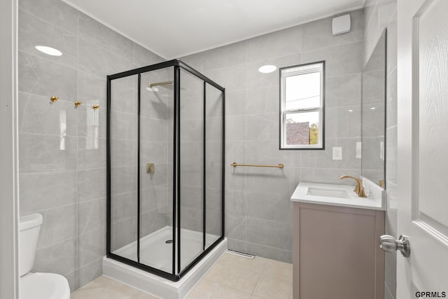 bathroom featuring vanity, a shower with door, tile walls, tile patterned flooring, and toilet