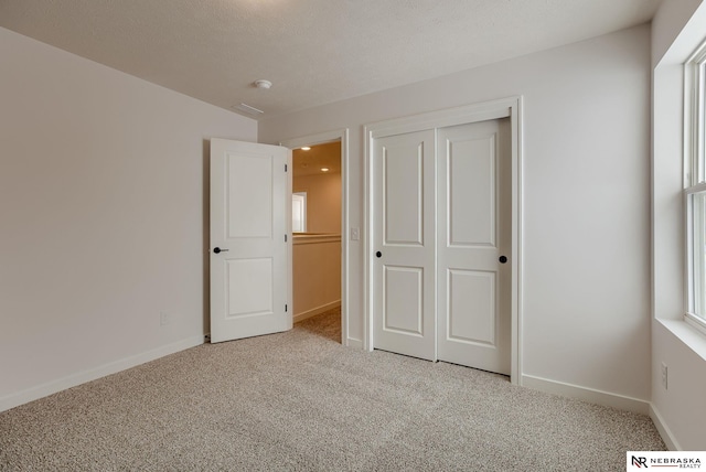 unfurnished bedroom featuring a textured ceiling, a closet, and light colored carpet