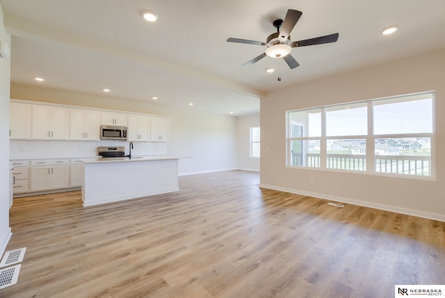 kitchen with a center island with sink, light wood-type flooring, appliances with stainless steel finishes, and white cabinetry