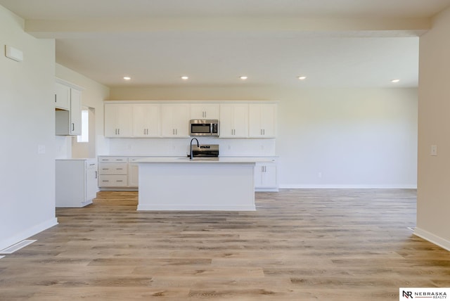 kitchen with a center island with sink, sink, light hardwood / wood-style flooring, white cabinetry, and stainless steel appliances