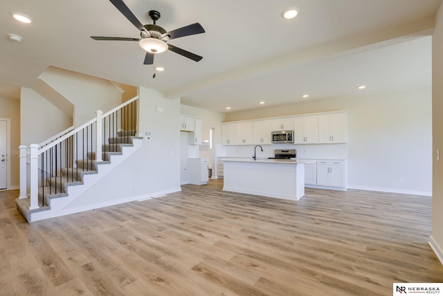 unfurnished living room featuring beamed ceiling, ceiling fan, sink, and light hardwood / wood-style flooring