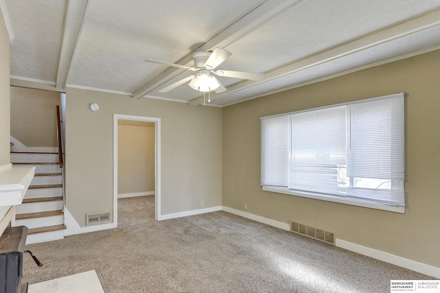 empty room featuring a textured ceiling, light colored carpet, ceiling fan, crown molding, and beamed ceiling