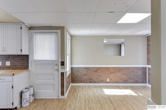 kitchen featuring white cabinetry, a drop ceiling, brick wall, butcher block countertops, and light wood-type flooring