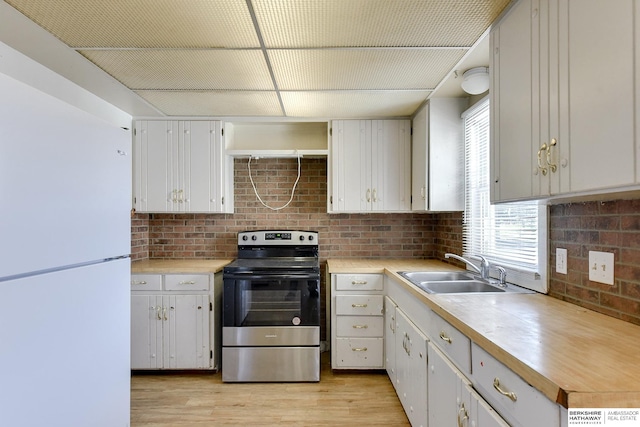 kitchen featuring electric range, white refrigerator, white cabinetry, and sink