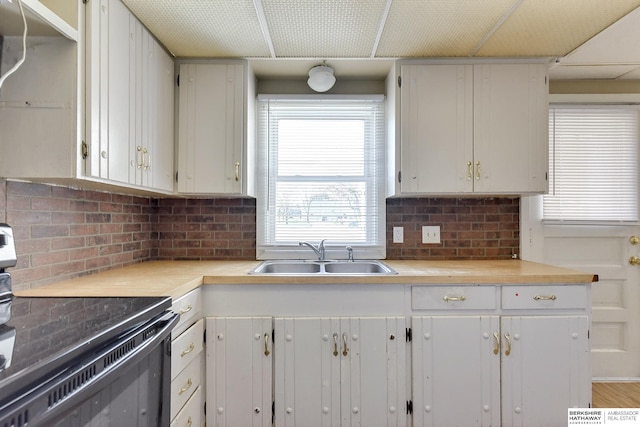 kitchen featuring backsplash, black range with electric cooktop, sink, hardwood / wood-style flooring, and white cabinetry