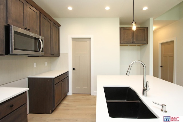 kitchen with hanging light fixtures, sink, dark brown cabinetry, and light hardwood / wood-style floors