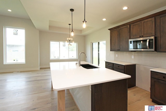 kitchen with dark brown cabinets, a tray ceiling, sink, and a center island with sink