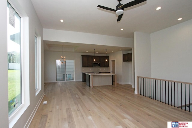 unfurnished living room with sink, ceiling fan with notable chandelier, and light hardwood / wood-style flooring