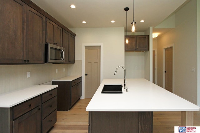 kitchen with sink, dark brown cabinets, a center island with sink, pendant lighting, and backsplash