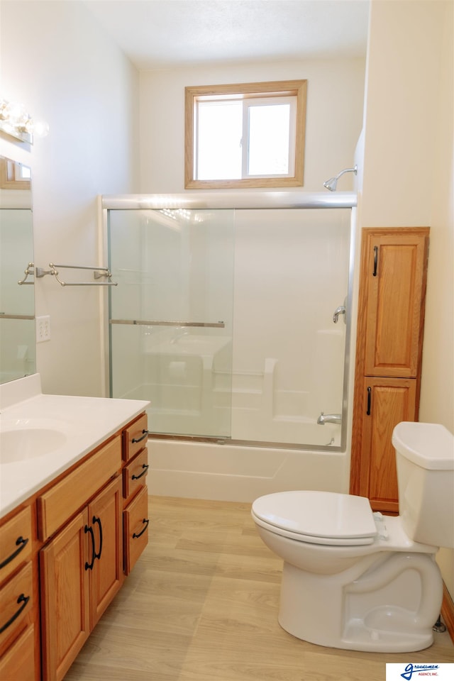 full bathroom with shower / bath combination with glass door, vanity, hardwood / wood-style flooring, and toilet