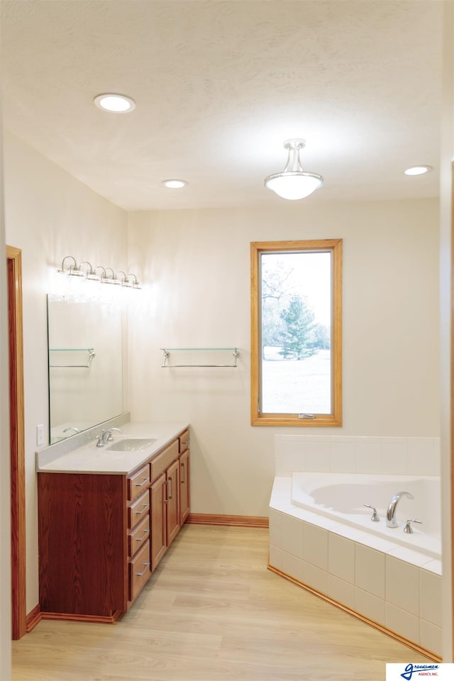 bathroom featuring vanity, wood-type flooring, and tiled tub