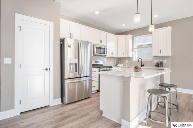 kitchen featuring stainless steel appliances, light hardwood / wood-style flooring, white cabinets, a center island, and hanging light fixtures