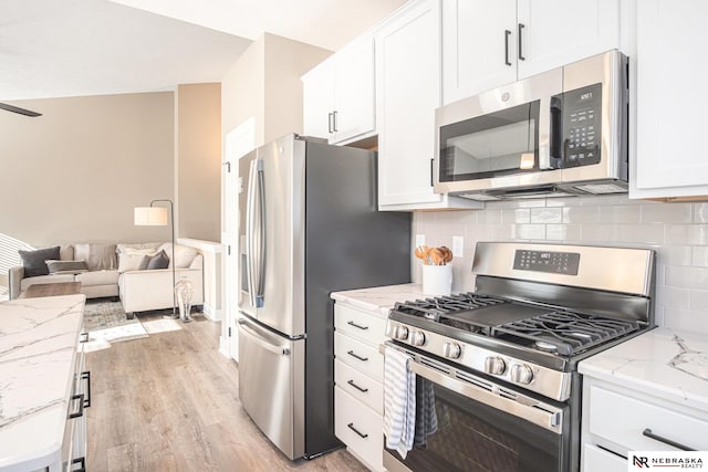 kitchen with light wood-type flooring, stainless steel appliances, white cabinetry, and light stone counters