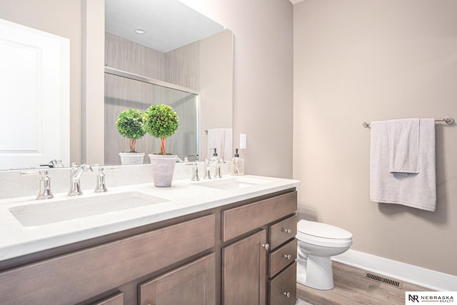 bathroom featuring vanity, wood-type flooring, a shower with shower door, and toilet