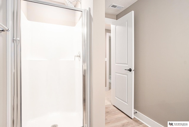 bathroom featuring hardwood / wood-style flooring, a shower with shower door, and a textured ceiling