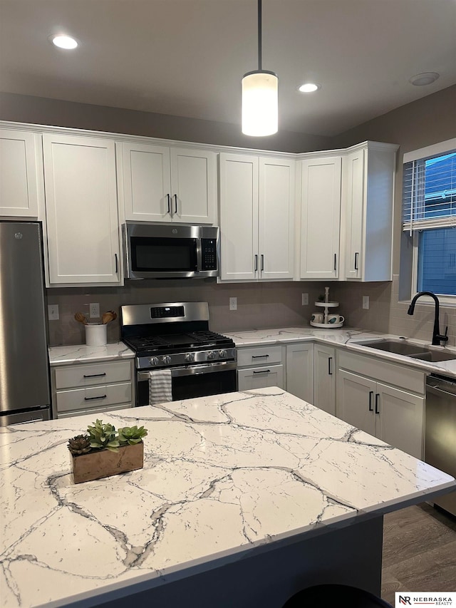 kitchen with white cabinets, sink, hanging light fixtures, wood-type flooring, and stainless steel appliances